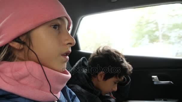 4k, slowmotion. bror och syster tvillingar, åka i baksätet på bilen och lyssna på musik i hörlurar. — Stockvideo