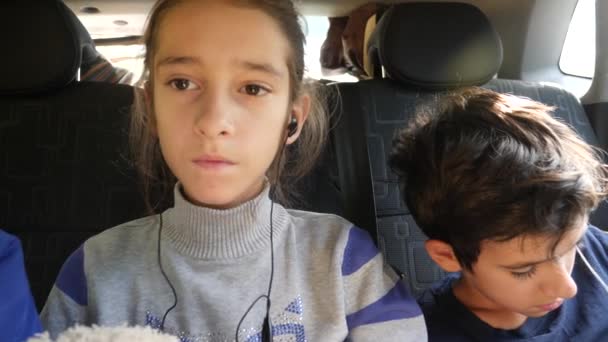 4k, Zeitlupe. Geschwister Zwillinge, fahren auf dem Rücksitz des Autos und hören Musik über Kopfhörer. — Stockvideo