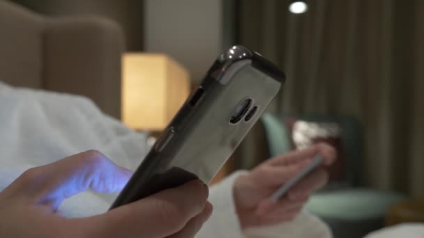 Koop online met uw smartphone en credit card. Vrouwelijke handen gebruiken de kaart en de telefoon in de avond in het appartement. 4k — Stockvideo