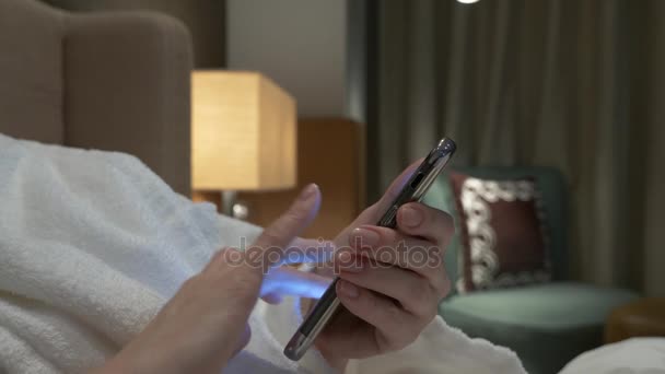 Vértes fiatal nő kezet gépelés sms telefon képek görgetés. női kezek használ egy smartphone, este az ágyban. 4k — Stock videók
