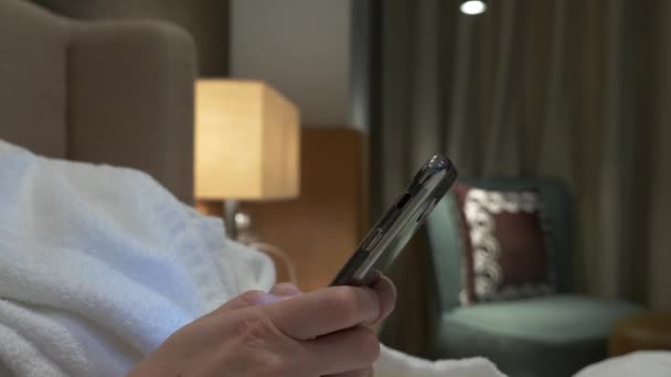 Nahaufnahme von jungen Frauenhänden, die SMS schreiben und Handyfotos scrollen. Frauenhände benutzen abends auf dem Bett ein Smartphone. 4k — Stockvideo