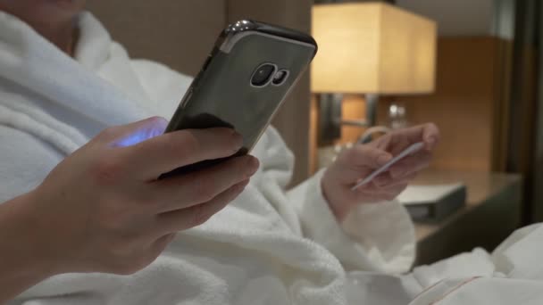 Acquista online con il tuo smartphone e carta di credito. Le mani femminili usano la carta e il telefono la sera nell'appartamento. 4k — Video Stock