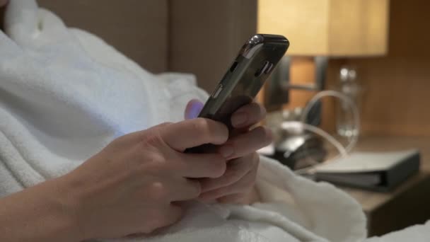 Nahaufnahme von jungen Frauenhänden, die SMS schreiben und Handyfotos scrollen. Frauenhände benutzen abends auf dem Bett ein Smartphone. 4k — Stockvideo
