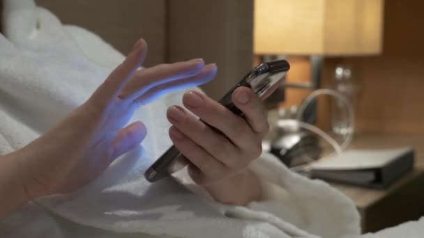 Nahaufnahme von jungen Frauenhänden, die SMS schreiben und Handyfotos scrollen. Frauenhände benutzen abends auf dem Bett ein Smartphone. 4k — Stockvideo