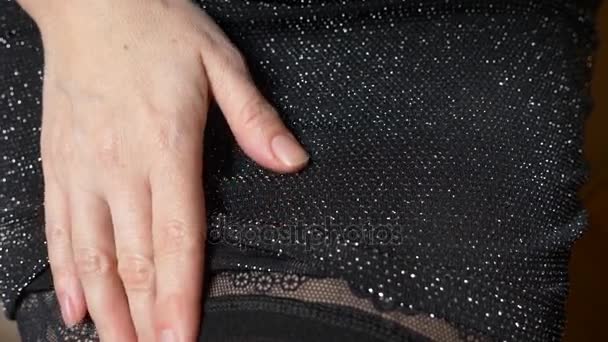 Женщина в маленьком черном платье регулирует чулок на ноге. 4k, slow motion — стоковое видео