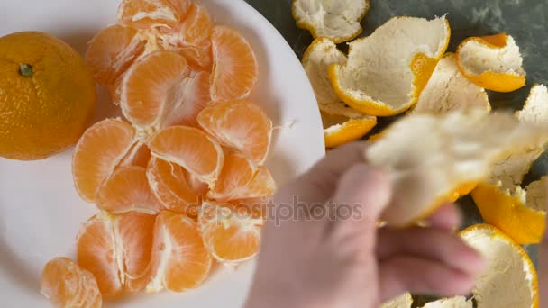 Женские руки чистят кожуру мандаринов, мандаринские ломтики складываются в миску. 4k, slow motion — стоковое видео