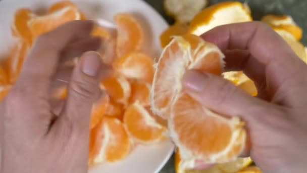 Женские руки чистят кожуру мандаринов, мандаринские ломтики складываются в миску. 4k, slow motion — стоковое видео