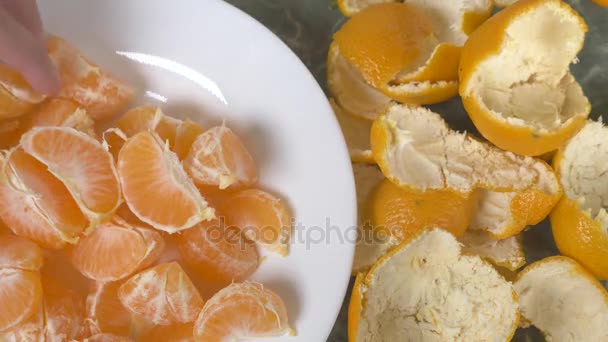 Жіночі руки очищають шкірку мандаринів, скибочки мандарина збирають у миску. 4k, повільний рух — стокове відео