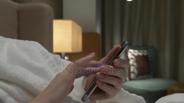 Крупный план молодой женщины руки печатая смс прокрутки фотографии телефона. женские руки используют смартфон вечером на кровати. 4k — стоковое видео