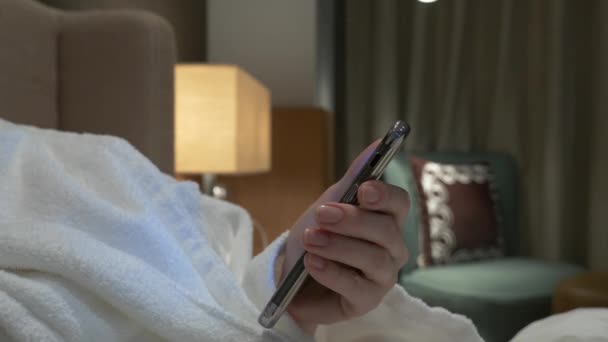 Primo piano di giovani mani donna digitando sms scorrimento foto telefoniche. le mani femminili usano uno smartphone la sera sul letto. 4k — Video Stock