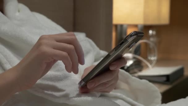 Close-up van jonge vrouw handen typen sms telefoon foto's scrollen. vrouwelijke handen gebruiken een smartphone in de avond op het bed. 4k — Stockvideo