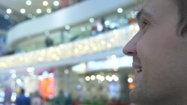 Profiel van de close-up van een man die naar de mensen in een modern winkelcentrum kijkt. Onscherpe achtergrond. 4k — Stockvideo