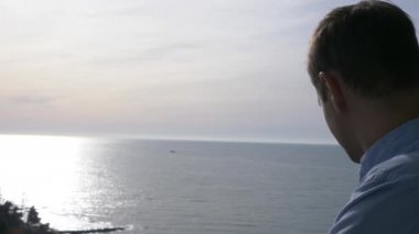 adam balkonda bir güneşli sabah üzerinde duruyor ve aşağı şehir ve sahil üzerinde görünüyor. 4k