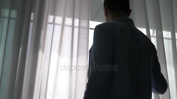 De man wordt geopend van een transparant gordijn op het venster en stapt uit op het balkon. 4k — Stockvideo