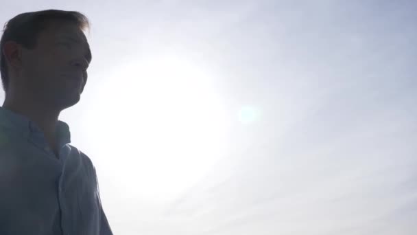 Muž stojí na balkóně na slunečné ráno a dívá se dolů na město a pobřeží. 4k — Stock video