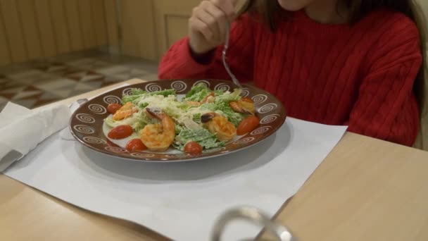Девушка в кафе ест салат Цезарь с креветками. 4k — стоковое видео