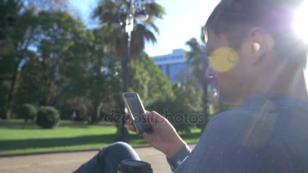 Zblízka se muže používat mobilní smartphone, venku. muž SMS na svůj smartphone na ulicích města za slunečného dne. 4k, pomalý pohyb — Stock video