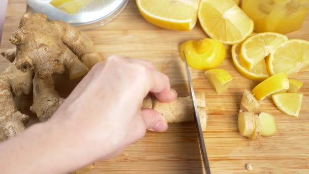 Mains féminines coupées en morceaux racine de gingembre pour une boisson à base d'agrumes faite à la main avec du gingembre. 4k, au ralenti — Video