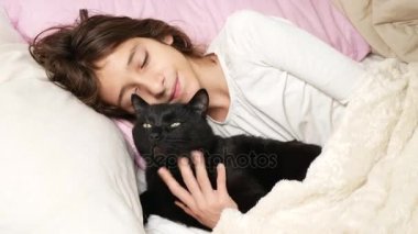 küçük bir kız hugs ve evde beslenen hayvan, kara kedi, yatakta yatan vuruş. 4k,