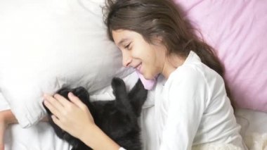 küçük bir kız hugs ve evde beslenen hayvan, kara kedi, yatakta yatan vuruş. 4k,