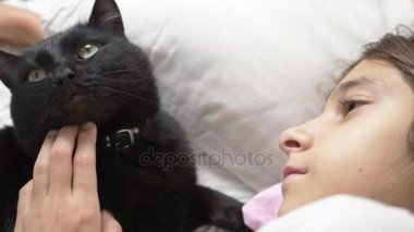 küçük bir kız hugs ve evde beslenen hayvan, kara kedi, yatakta yatan vuruş. 4k,