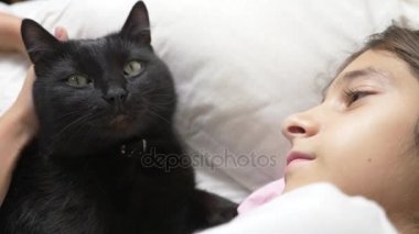 küçük bir kız hugs ve evde beslenen hayvan, kara kedi, yatakta yatan vuruş. 4k,