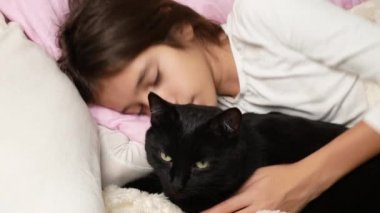 küçük bir kız hugs ve evde beslenen hayvan, kara kedi, yatakta yatan vuruş. 4k,