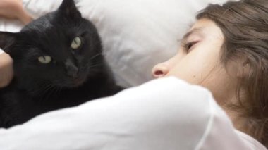 küçük bir kız hugs ve evde beslenen hayvan, kara kedi, yatakta yatan vuruş. 4k,