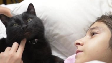 küçük bir kız hugs ve evde beslenen hayvan, kara kedi, yatakta yatan vuruş. 4k,