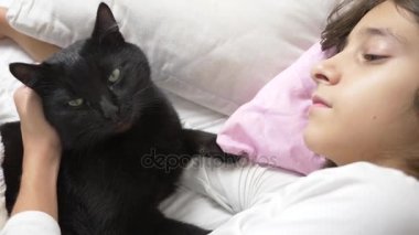 küçük bir kız hugs ve evde beslenen hayvan, kara kedi, yatakta yatan vuruş. 4k,