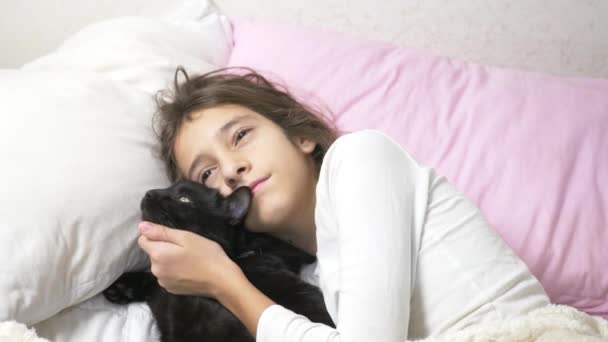 Ein kleines Mädchen umarmt und streichelt ihr Haustier, eine schwarze Katze, die im Bett liegt. 4k, — Stockvideo