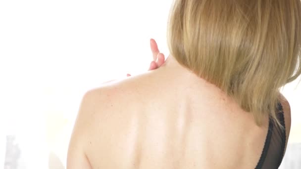 Back view, close-up, 4k, slow-motion. a blonde woman takes off a bra strap with one shoulder. — Stock Video