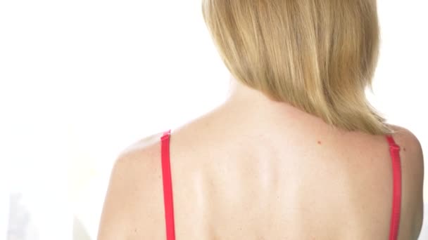 Vue arrière, gros plan, 4k, ralenti. une femme blonde enlève une sangle de soutien-gorge avec une épaule . — Video
