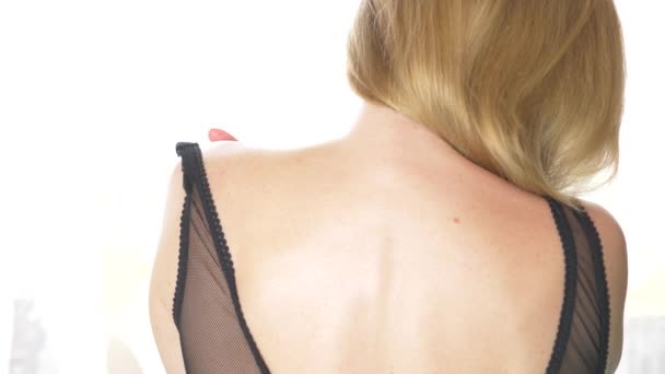 Vista traseira, close-up, 4k, câmera lenta. uma mulher loira tira uma alça de sutiã com um ombro . — Vídeo de Stock