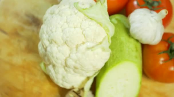 Coliflor, calabacín, tomate y ajo, girando sobre una tabla de cortar de madera. 4k . — Vídeos de Stock