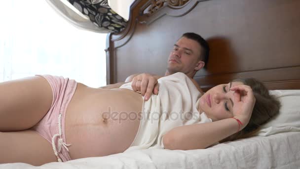 Bela, jovem grávida acariciando sua barriga deitada na cama. 4K. Movimento lento — Vídeo de Stock