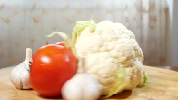 Couve-flor e três tomates girando em uma tábua de corte de madeira. 4k — Vídeo de Stock