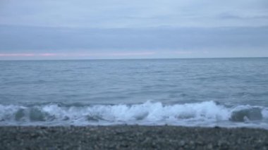 Çakıl plajı gün batımında. Dalgalar sıçramak ve damlacıklar kesin. 4k, ağır çekim