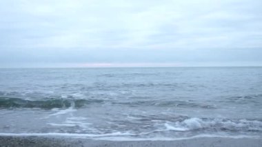 Çakıl plajı gün batımında. Dalgalar sıçramak ve damlacıklar kesin. 4k, ağır çekim