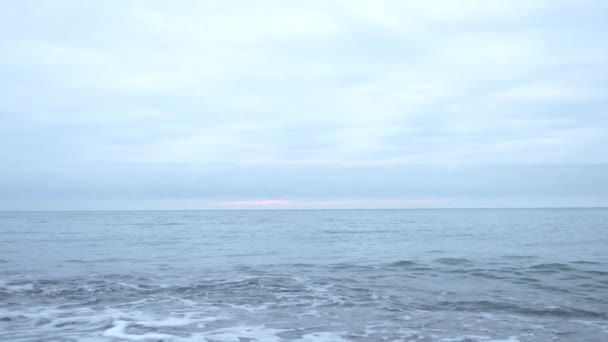 Kiezelstrand bij zonsondergang. De golven splatter en breken in druppeltjes. 4k, slow-motion — Stockvideo