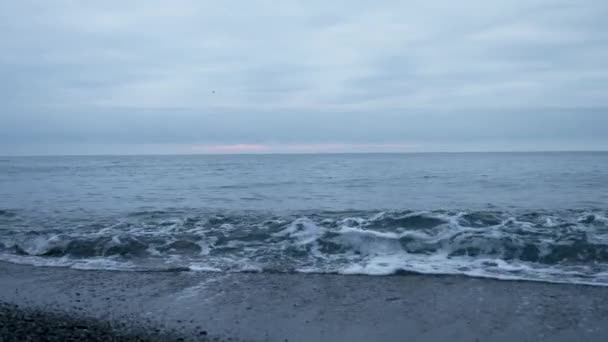 Kavicsos strand, naplementekor. A hullámok fröccs, és cseppek betörni. 4k, lassú mozgás — Stock videók