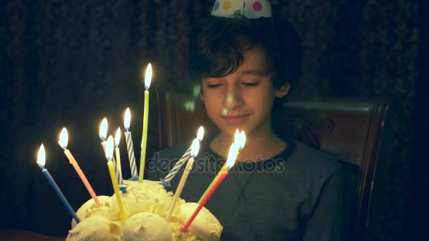 Мальчик загадывает желание и смотрит на свечи на торте в темной комнате. 4k, slow-motion — стоковое видео