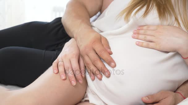 一个美丽的年轻孕妇和她的肌肉丈夫躺在床上, 丈夫正在熨他的妻子的肚子。4k、慢动作 — 图库视频影像