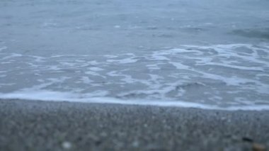 Çakıl plajı gün batımında. Dalgalar sıçramak ve damlacıklar kesin. 4k, ağır çekim