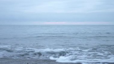 Çakıl plajı gün batımında. Dalgalar sıçramak ve damlacıklar kesin. 4k, ağır çekim