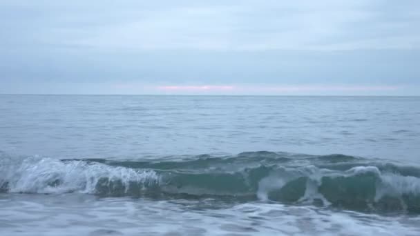 Kiezelstrand bij zonsondergang. De golven splatter en breken in druppeltjes. 4k, slow-motion — Stockvideo