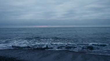 Çakıl plajı gün batımında. Dalgalar sıçramak ve damlacıklar kesin. 4k, ağır çekim