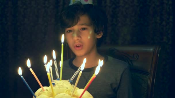 Pojken gör en önskan och ser på ljusen på tårtan i det mörka rummen. 4k, pojken blåser ut ljusen. Slow motion — Stockvideo