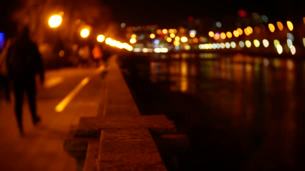 Άνθρωποι κάνουν βόλτα κατά μήκος ανάχωμα σπαρμένος με φώτα το βράδυ. θαμπάδα. 4 k bokeh — Αρχείο Βίντεο