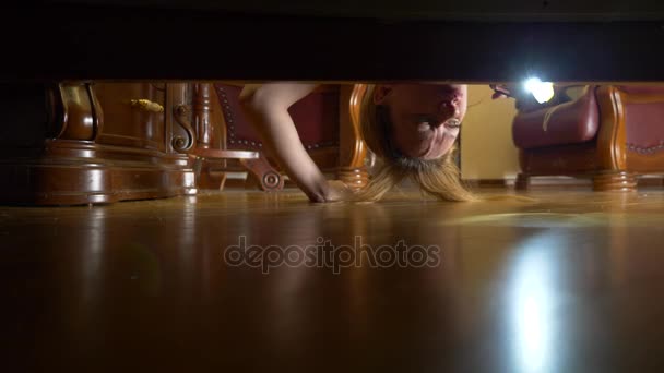 4K, câmara lenta, vista de baixo da cama. Uma mulher com uma lanterna está à procura de algo debaixo da cama . — Vídeo de Stock